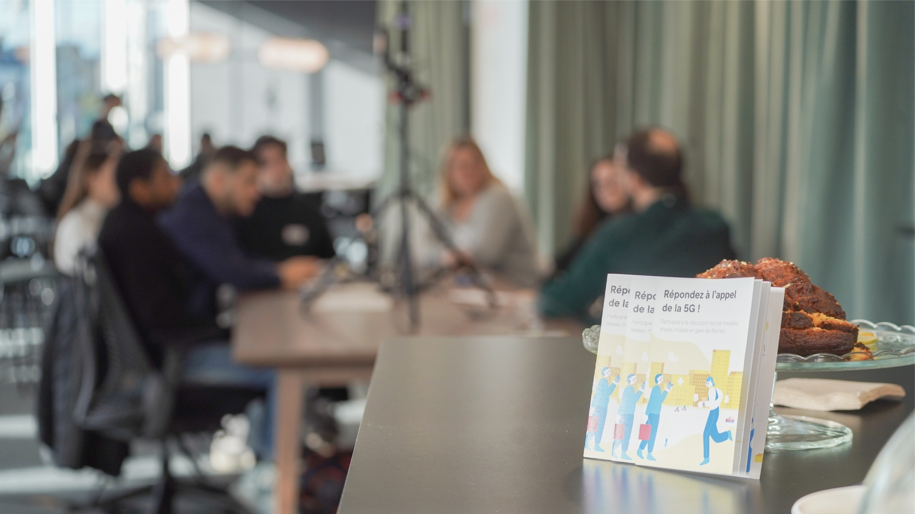 livrets en premier plan et des personnes qui débatent autour d'une table en arrière plan